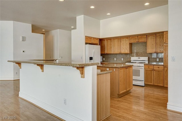 kitchen with backsplash, a center island with sink, light wood-type flooring, a kitchen bar, and white appliances