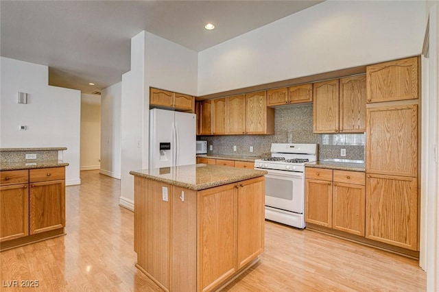 kitchen with white appliances, light stone counters, light wood-style floors, and a kitchen island