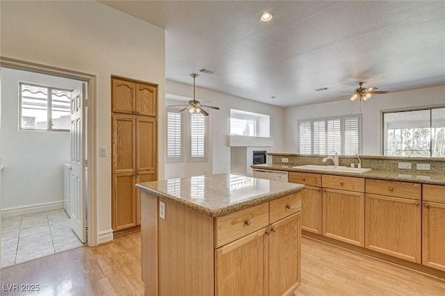 kitchen with light wood finished floors, a center island, ceiling fan, and a sink