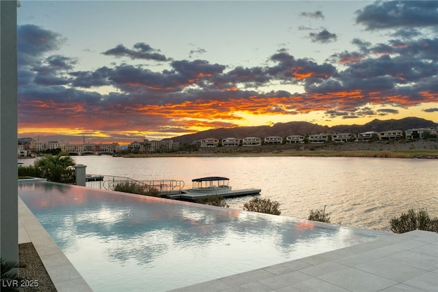 pool at dusk with a water view and a boat dock