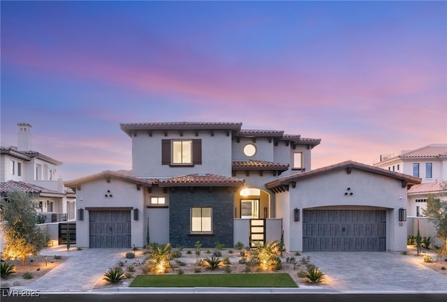 mediterranean / spanish-style home featuring a tile roof, decorative driveway, a garage, and stucco siding