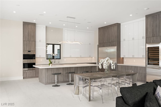 kitchen with a breakfast bar, light countertops, stainless steel appliances, white cabinetry, and modern cabinets