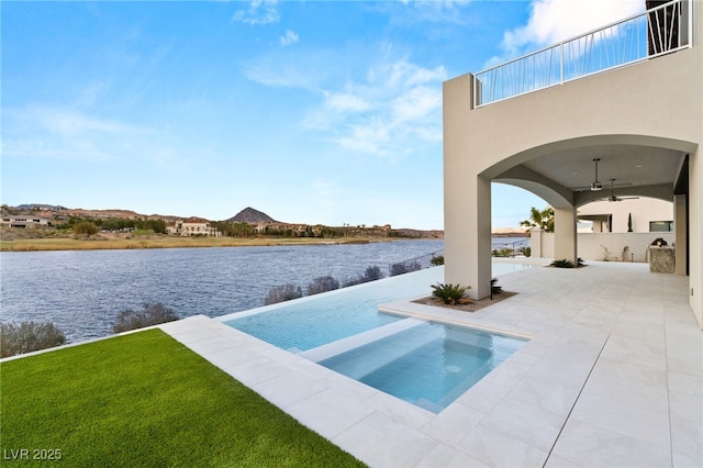 view of pool with a water view, a lawn, a ceiling fan, and a patio area