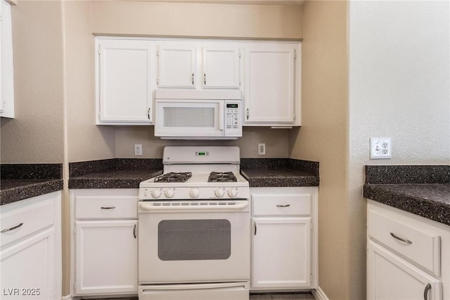 kitchen with white appliances, dark countertops, and white cabinetry