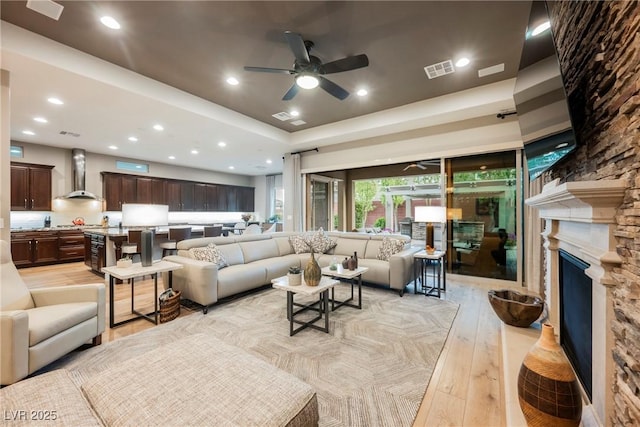 living area featuring visible vents, recessed lighting, light wood-style floors, a stone fireplace, and a raised ceiling