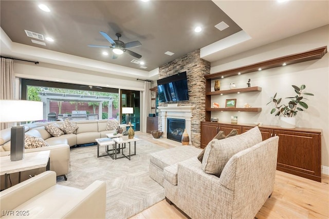 living area with a tray ceiling, light wood-style floors, visible vents, and a fireplace