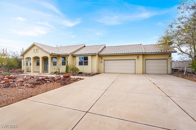 view of front of property featuring fence, driveway, stucco siding, a garage, and a tiled roof