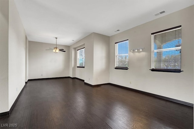 empty room featuring wood finished floors, visible vents, a wealth of natural light, and baseboards