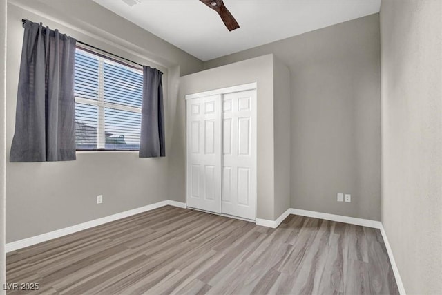 unfurnished bedroom featuring wood finished floors, baseboards, a closet, and ceiling fan