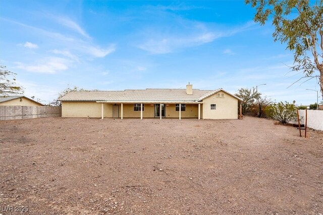 back of house with a chimney, a tile roof, stucco siding, and fence private yard