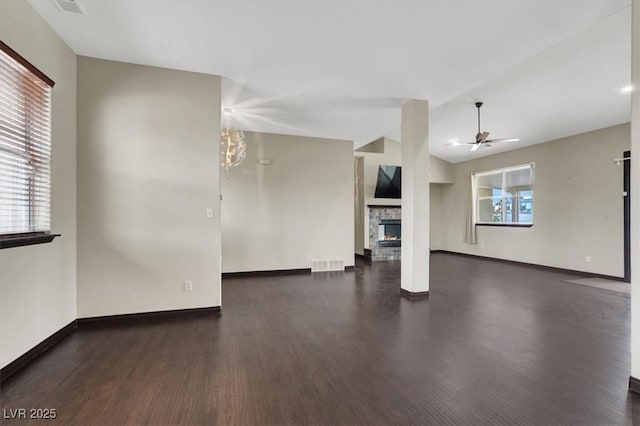 unfurnished living room with a stone fireplace, plenty of natural light, ceiling fan with notable chandelier, and visible vents