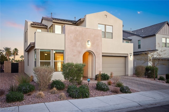 view of front facade featuring a tile roof, stucco siding, decorative driveway, a balcony, and an attached garage