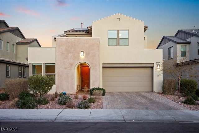 view of front facade featuring stucco siding, an attached garage, decorative driveway, and solar panels