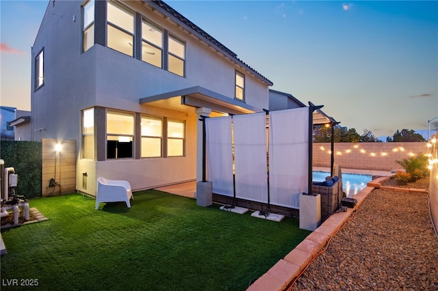 back of property at dusk with a yard, stucco siding, a fenced backyard, and a fenced in pool