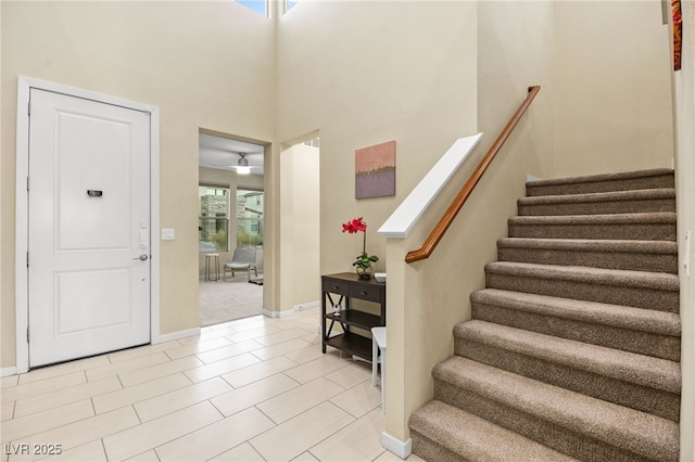 foyer featuring stairway, baseboards, a towering ceiling, and ceiling fan