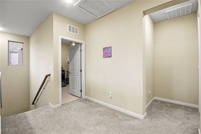 hall with attic access, an upstairs landing, visible vents, and carpet floors