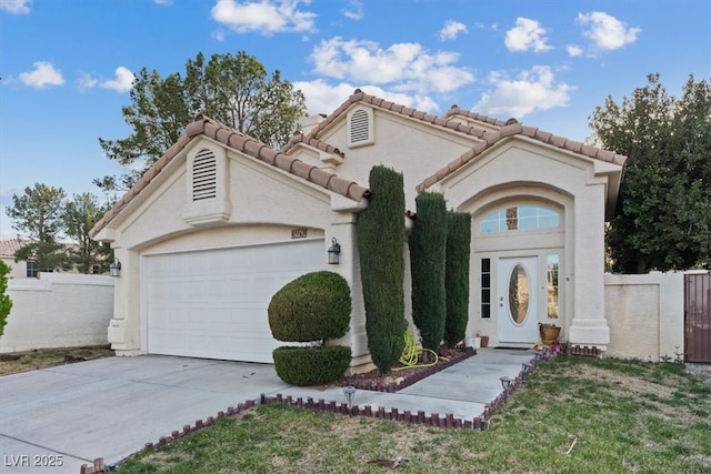 mediterranean / spanish house with fence, a tile roof, concrete driveway, stucco siding, and an attached garage