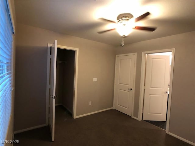 unfurnished bedroom with a walk in closet, baseboards, ceiling fan, dark carpet, and a closet