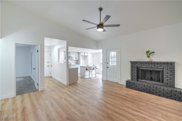 unfurnished living room featuring ceiling fan, a fireplace, baseboards, and light wood-style floors