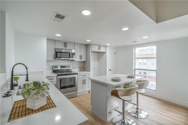 kitchen featuring visible vents, light countertops, light wood-type flooring, appliances with stainless steel finishes, and a kitchen breakfast bar