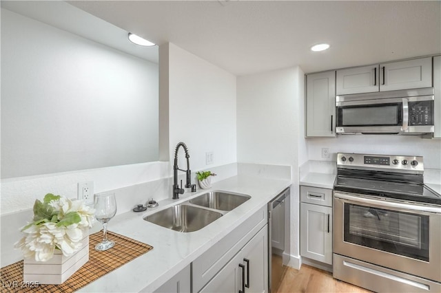 kitchen featuring light wood-style flooring, gray cabinets, a sink, light countertops, and appliances with stainless steel finishes