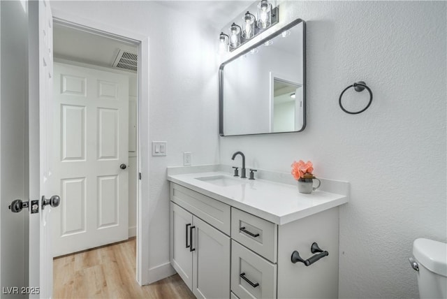 half bath with visible vents, toilet, vanity, and wood finished floors