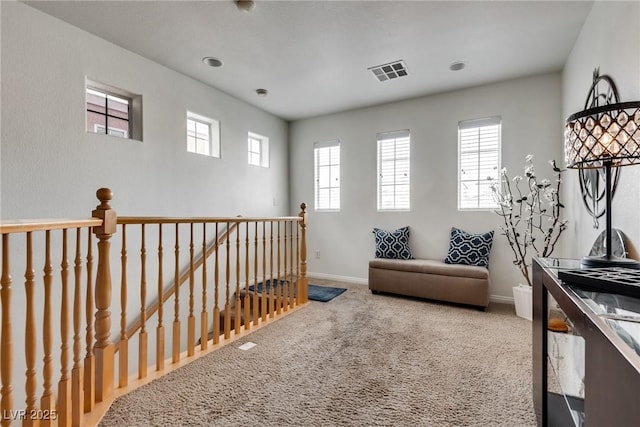 sitting room with carpet flooring, an upstairs landing, visible vents, and plenty of natural light