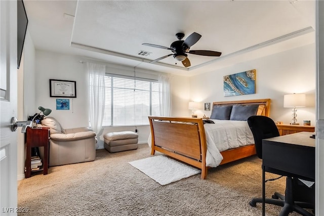 carpeted bedroom featuring a tray ceiling, a ceiling fan, visible vents, and baseboards