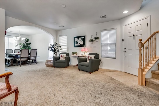 carpeted living room with stairway, arched walkways, visible vents, and an inviting chandelier