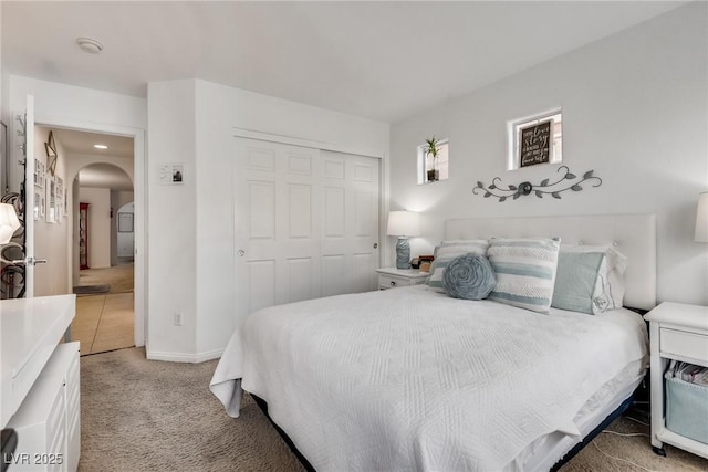 bedroom with arched walkways, baseboards, light carpet, and a closet