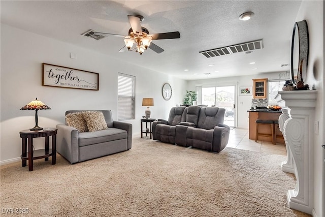 living area featuring visible vents, light carpet, a textured ceiling, and a ceiling fan