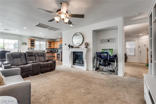 living room with a glass covered fireplace, recessed lighting, visible vents, and light carpet