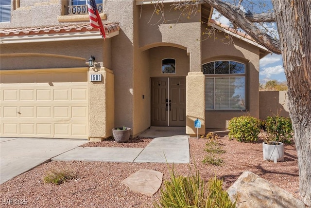 view of exterior entry featuring stucco siding, a tiled roof, and a garage