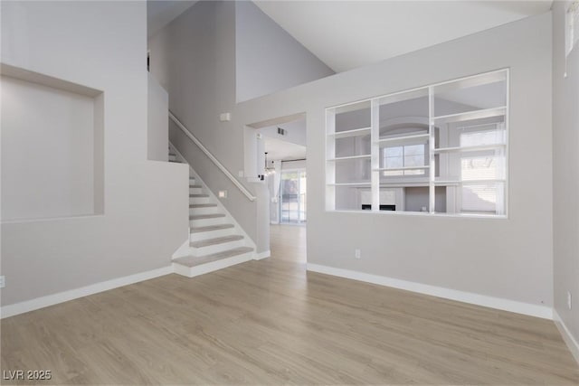 interior space featuring stairway, wood finished floors, baseboards, and high vaulted ceiling