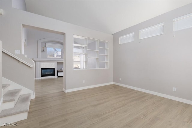 unfurnished living room with stairs, a glass covered fireplace, baseboards, and light wood-type flooring