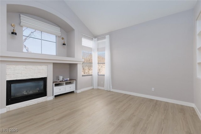 unfurnished living room featuring baseboards, a stone fireplace, wood finished floors, and vaulted ceiling