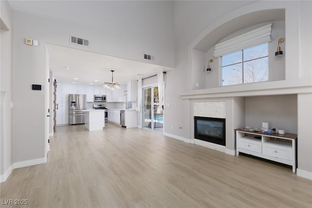 unfurnished living room featuring an inviting chandelier, light wood-style floors, and visible vents