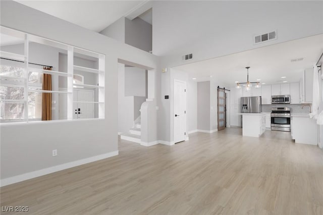 unfurnished living room with visible vents, baseboards, light wood-style floors, and a barn door