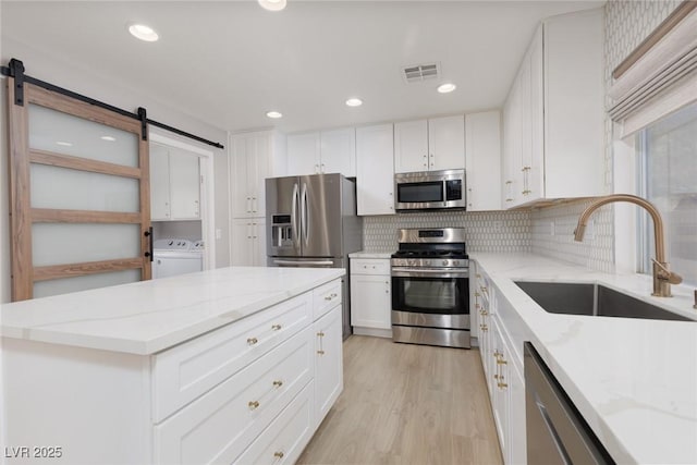 kitchen with white cabinets, stainless steel appliances, a barn door, and a sink