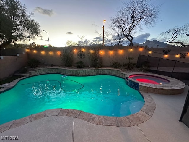 pool at dusk with a fenced backyard and a pool with connected hot tub