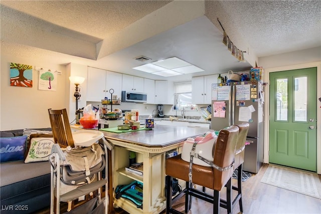 5706 W Lake Mead Blvd, Las Vegas, NV 89108 - kitchen with appliances with stainless steel finishes, a textured ceiling, white cabinetry, a breakfast bar area, and light wood-type flooring