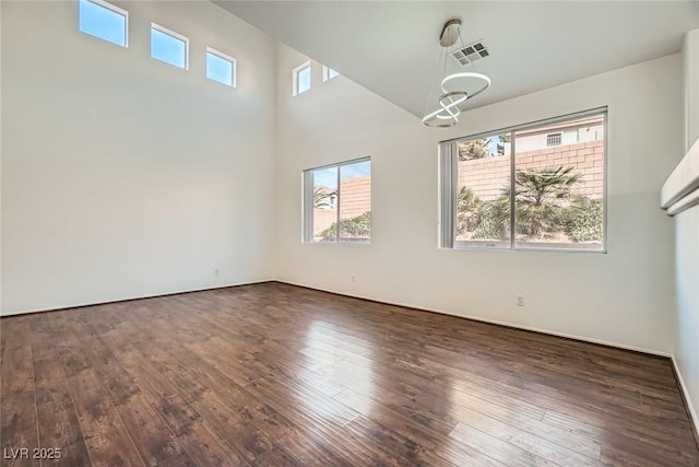 unfurnished room with a high ceiling, visible vents, dark wood-type flooring, and a healthy amount of sunlight