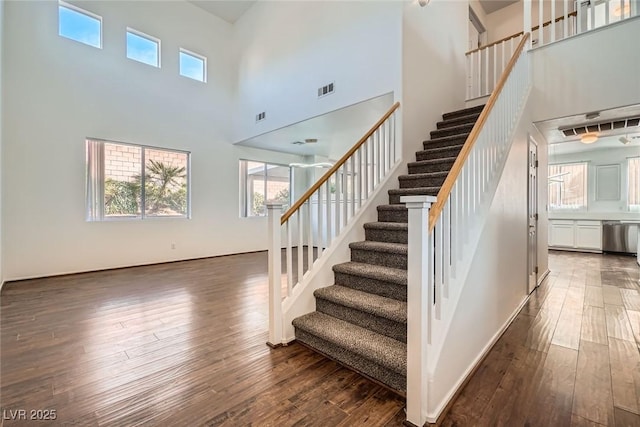 staircase featuring visible vents, a towering ceiling, and wood-type flooring