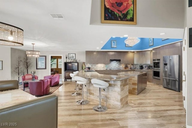 kitchen with visible vents, open floor plan, appliances with stainless steel finishes, a breakfast bar area, and decorative backsplash