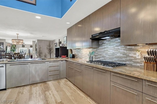 kitchen featuring under cabinet range hood, a sink, tasteful backsplash, light wood finished floors, and stainless steel gas cooktop