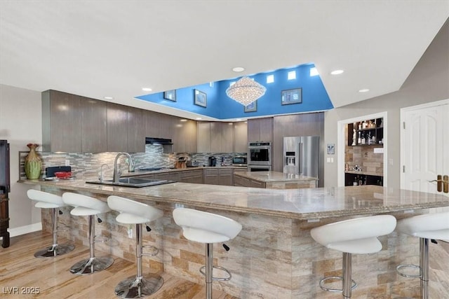 kitchen featuring a breakfast bar, a peninsula, a sink, appliances with stainless steel finishes, and tasteful backsplash