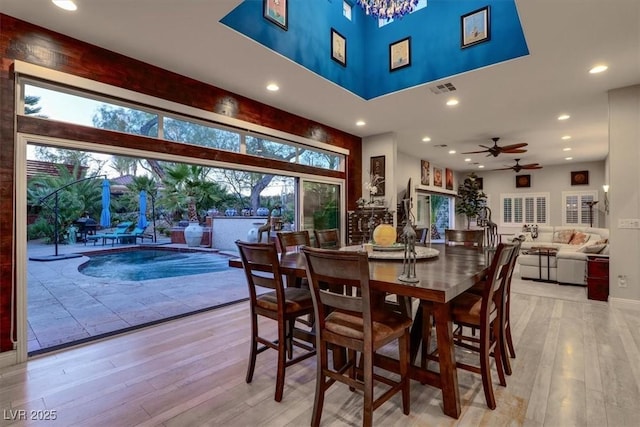 dining area featuring visible vents, ceiling fan with notable chandelier, recessed lighting, light wood finished floors, and a towering ceiling