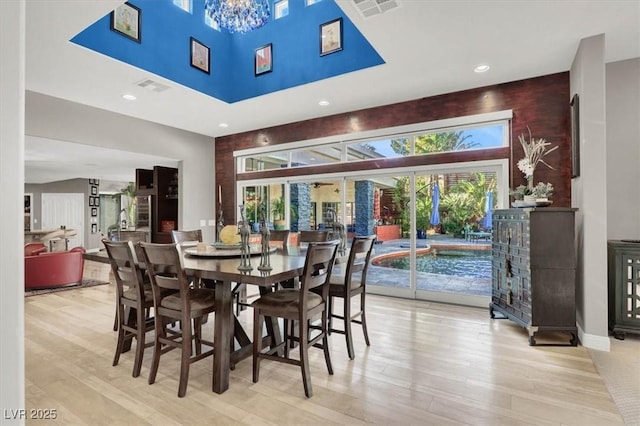 dining space featuring visible vents, light wood-style floors, and a towering ceiling