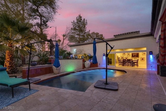 pool at dusk with an outdoor pool, outdoor dining area, and a patio