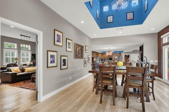 dining space with light wood-type flooring, recessed lighting, a high ceiling, an inviting chandelier, and baseboards